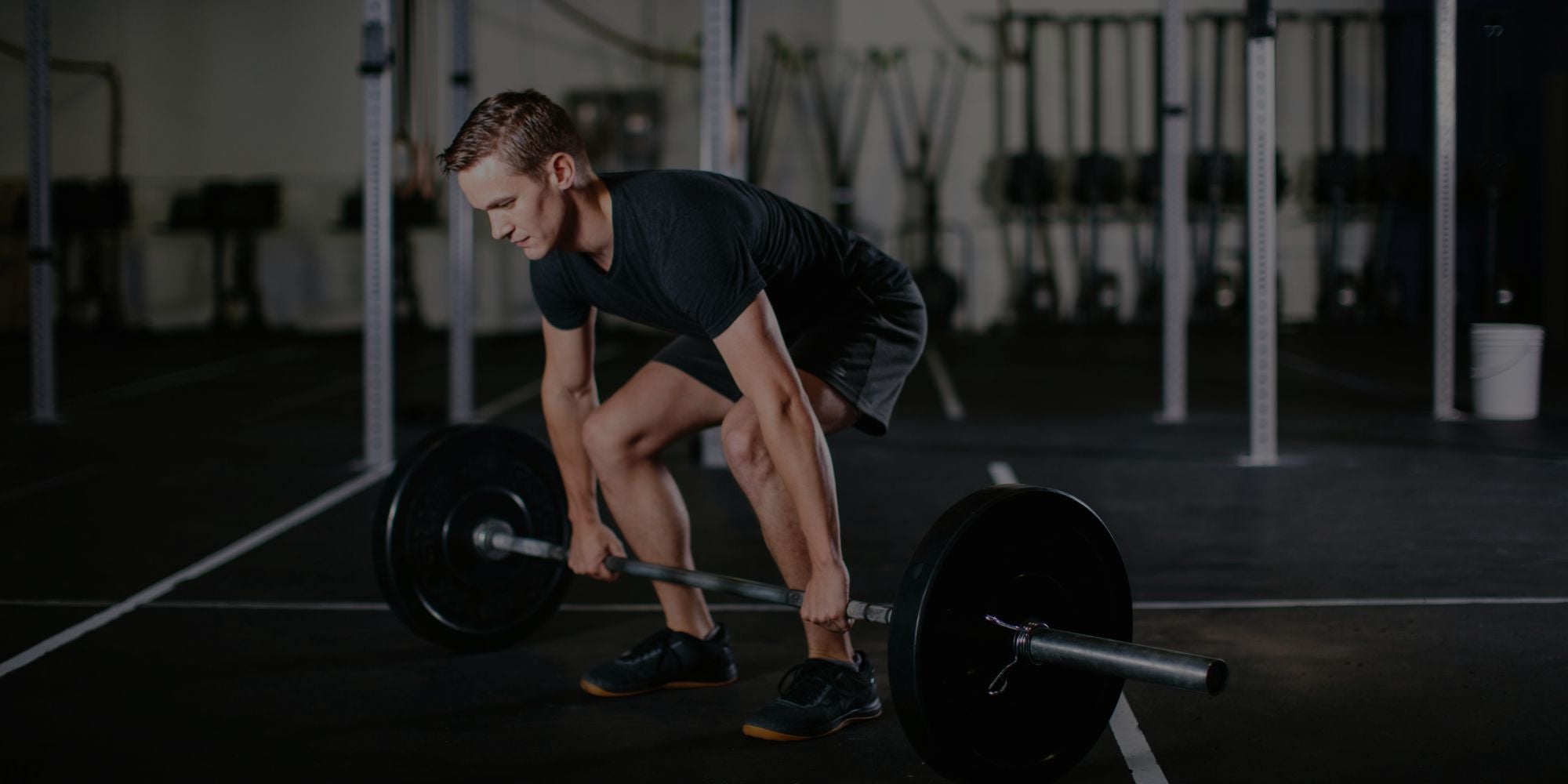 Athletic man lifting heavy barbell during deadlift workout in dark gym