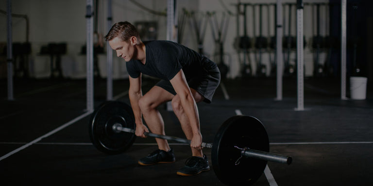 Athletic man lifting heavy barbell during deadlift workout in dark gym
